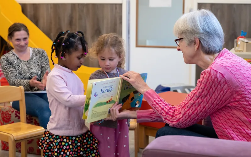 Een voorlezer leest voor aan twee jonge kinderen