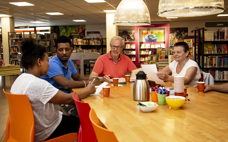 Anderstalige inwoners praten samen aan een tafel in de bibliotheek
